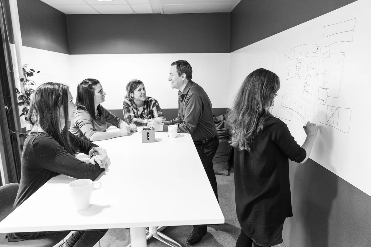 Kollegaer i workshop ved et bord og en tavle i 2016